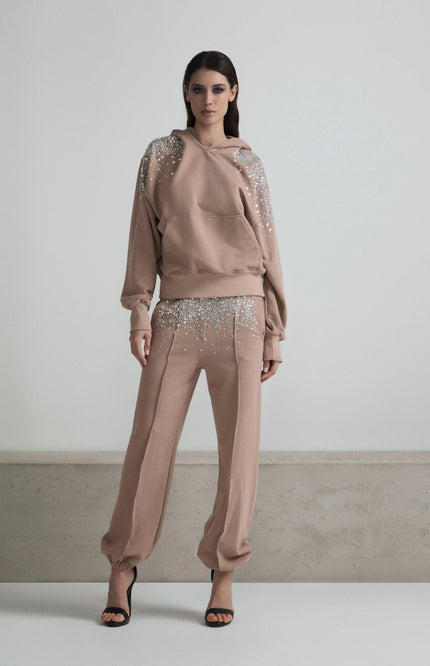 Woman in beige embellished sweatshirt and pants, standing indoors, fashion look