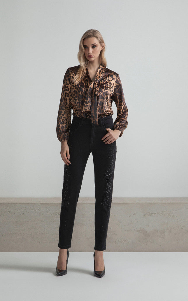 Woman wearing leopard print blouse and black embellished pants, standing indoors