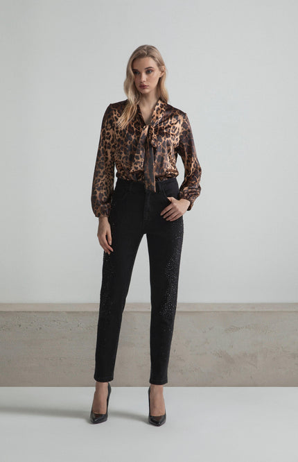 Woman wearing leopard print blouse and black embellished pants, standing indoors