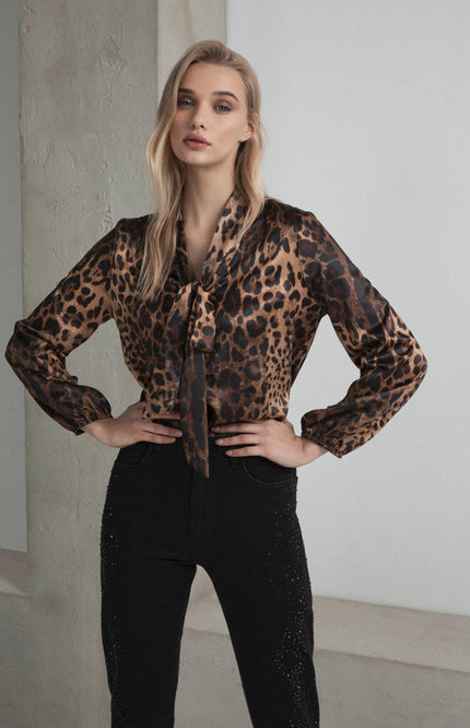 Woman wearing a leopard print blouse and black high-waisted pants, standing indoors