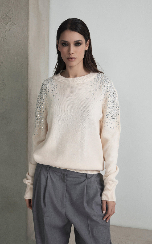 Woman wearing cream embellished sweater and grey trousers in minimal setting