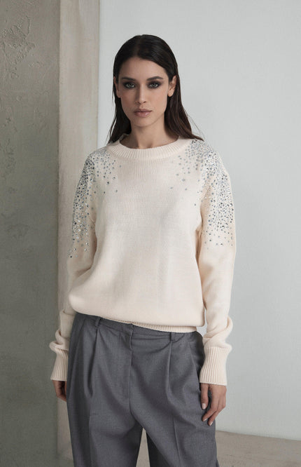 Woman wearing cream embellished sweater and grey trousers in minimal setting