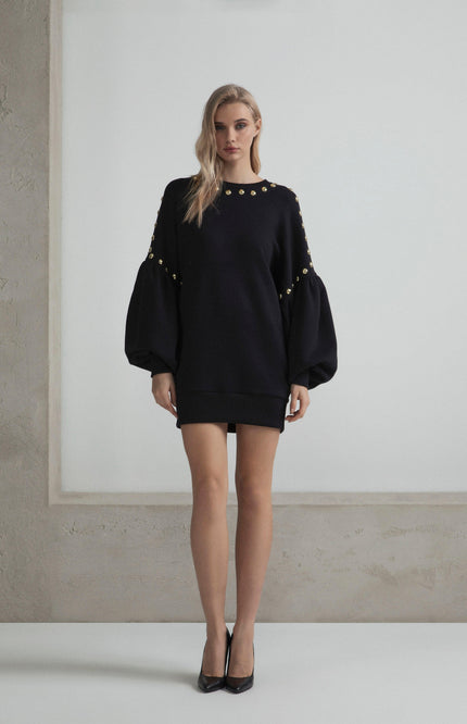 Woman wearing black mini dress with gold button details and balloon sleeves