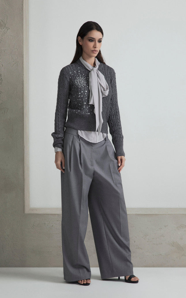 Woman in a grey sequin sweater, wide-leg trousers and bow blouse, standing indoors