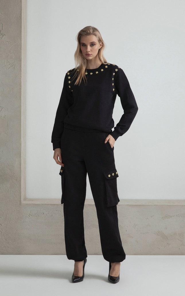 Woman wearing black sweatshirt and cargo pants with gold button details in minimalist setting