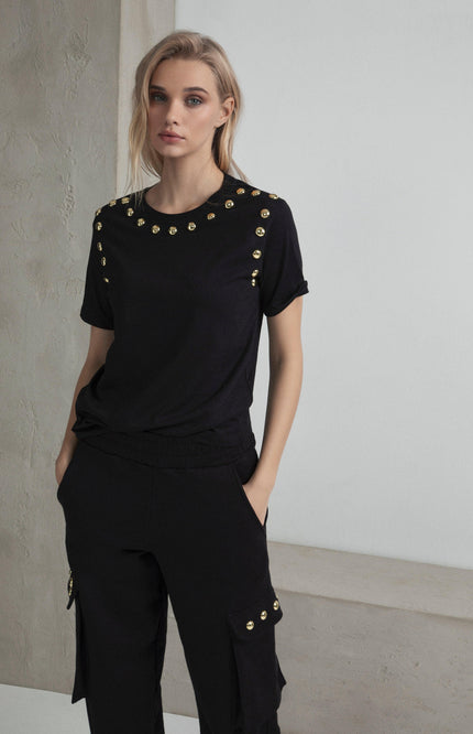 Woman in black t-shirt and pants with gold studs, modern fashion style, neutral background