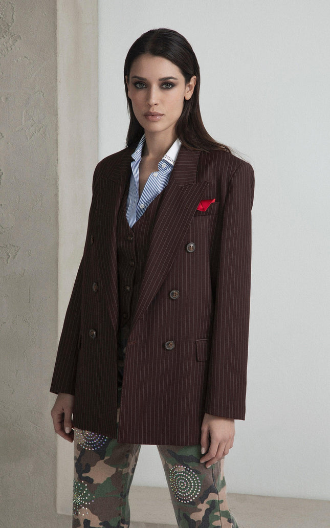 Woman wearing a brown pinstripe blazer, striped shirt, and camo pants with colorful details