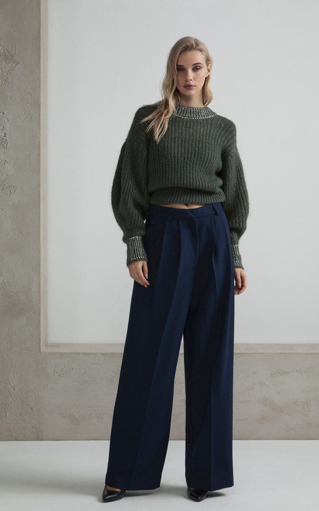 Woman in chunky green sweater with crystal cuffs and navy wide-leg trousers