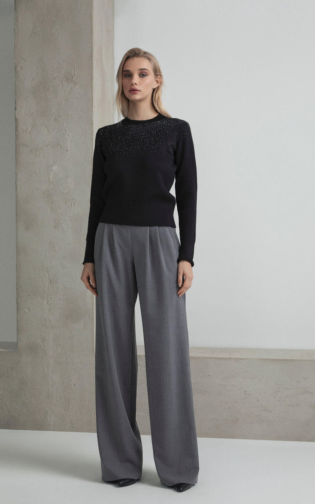 Woman wearing a black embellished sweater and wide-leg gray trousers, minimalist setting