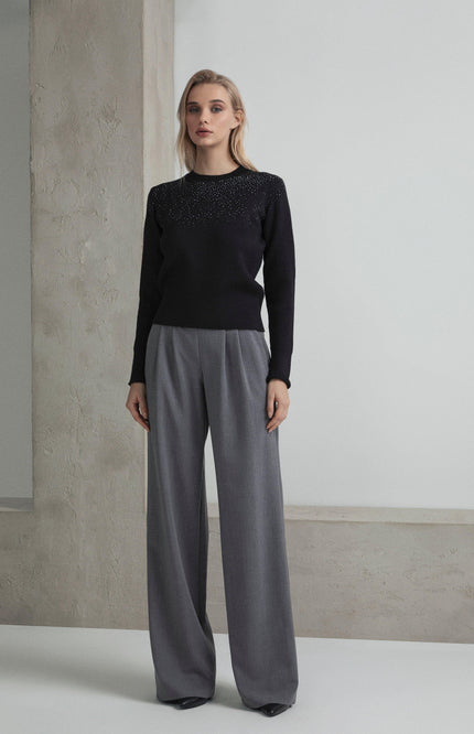 Woman wearing a black embellished sweater and wide-leg gray trousers, minimalist setting