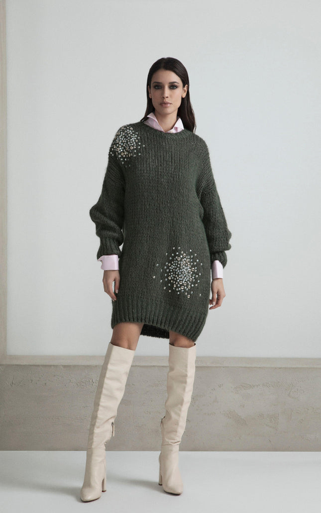 Woman in a dark green embellished sweater dress with long sleeves and white knee-high boots