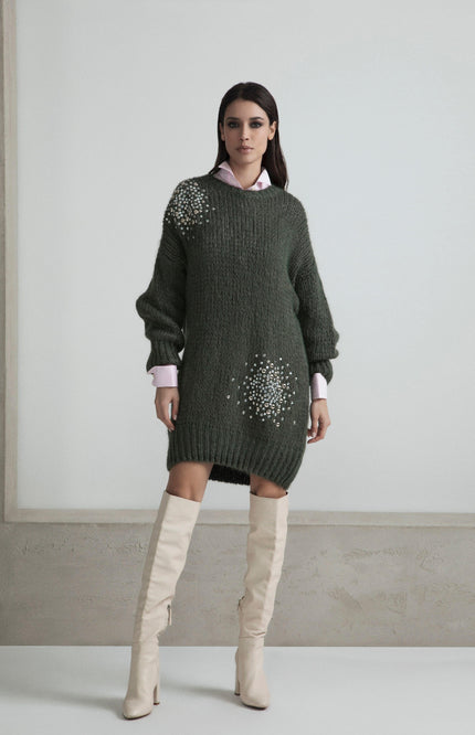 Woman in a dark green embellished sweater dress with long sleeves and white knee-high boots