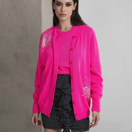 Woman wearing bright pink embellished cardigan, pink top, and black polka dot shorts