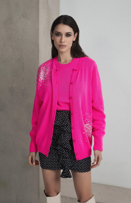 Woman wearing bright pink embellished cardigan, pink top, and black polka dot shorts