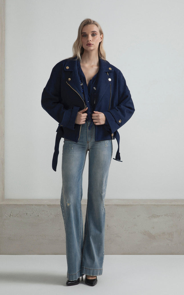 Woman in a navy oversized jacket and flared jeans, standing in a minimalist room