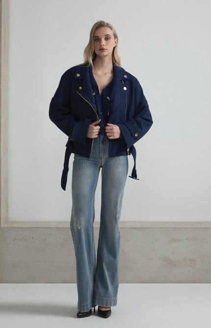 Woman in a navy oversized jacket and flared jeans, standing in a minimalist room