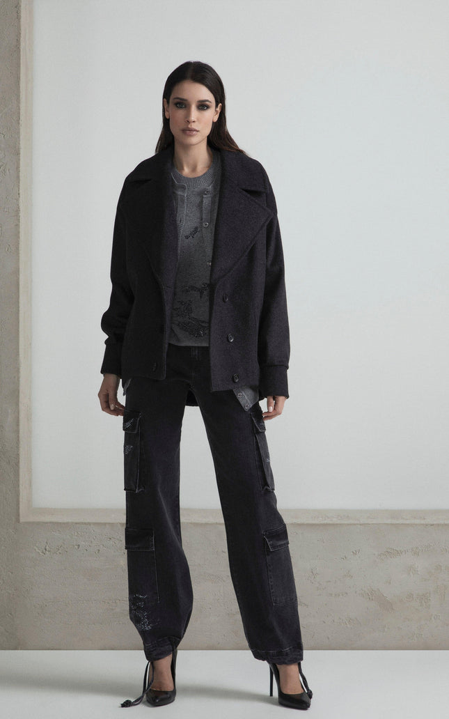 Woman wearing a dark oversized jacket, cargo pants, and heels in a minimalist setting