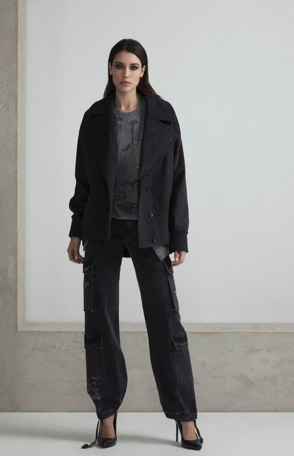 Woman wearing a dark oversized jacket, cargo pants, and heels in a minimalist setting