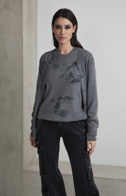 Woman wearing a grey sweater set with sequin details and black cargo jeans in a minimalist room
