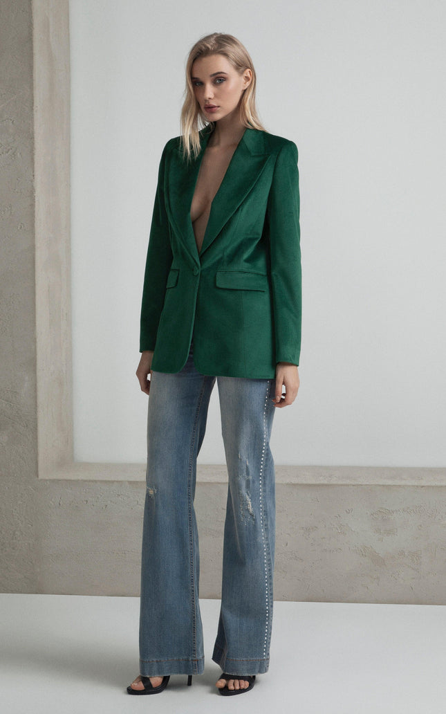 Woman wearing green tailored blazer and wide-leg distressed jeans, standing indoors