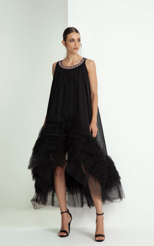 Woman wearing a black sleeveless dress with ruffled hem and jeweled neckline, high heels