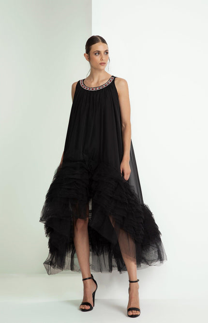 Woman wearing a black sleeveless dress with ruffled hem and jeweled neckline, high heels