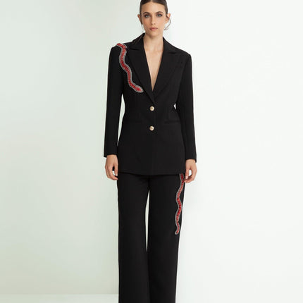 Woman in a black tailored suit with red sequin snake detail, wide leg pants, minimalist setting