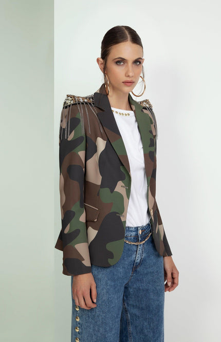 Woman wearing camo print blazer with jeweled shoulders, white top, and blue jeans.