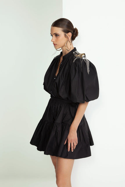 Woman in short black puff sleeve dress with embellished shoulder, side view, fashion look