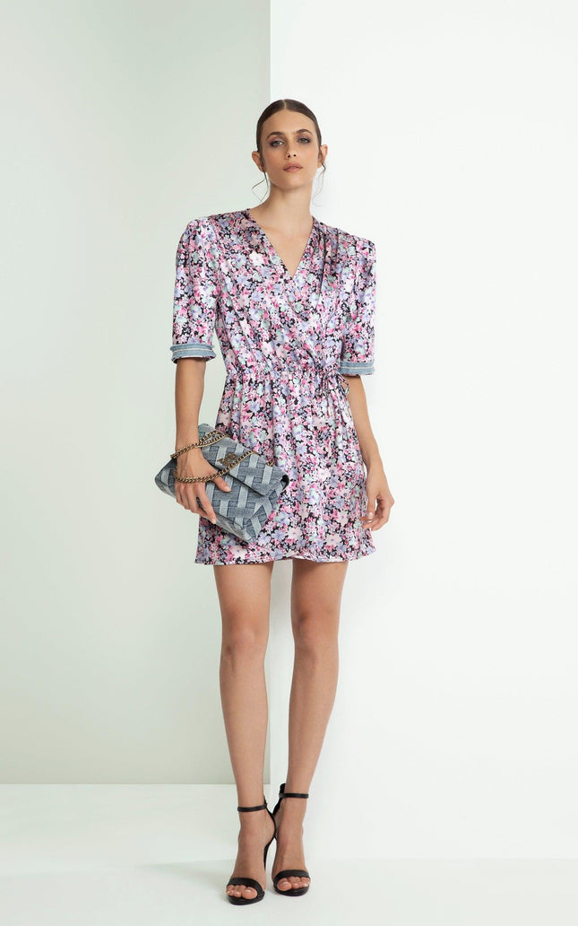 Woman wearing a short floral wrap dress with a V-neck, holding a woven clutch bag