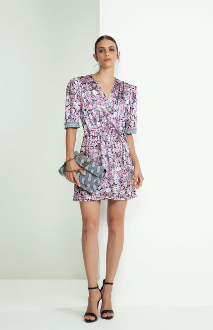 Woman wearing a short floral wrap dress with a V-neck, holding a woven clutch bag