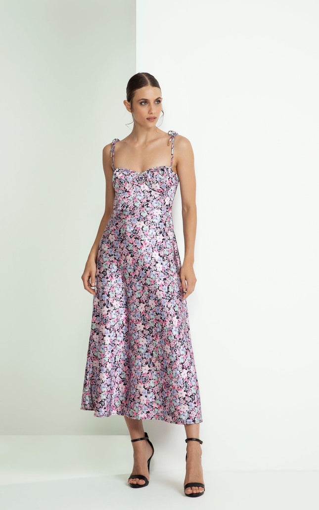 Woman in a sleeveless floral midi dress with tie straps, standing against a white background