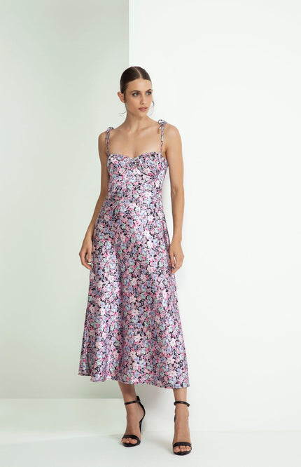 Woman in a sleeveless floral midi dress with tie straps, standing against a white background