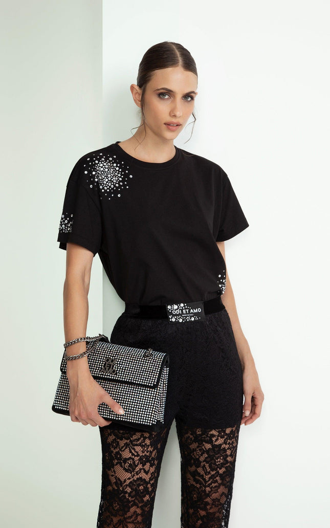 Woman wearing black crystal-studded t-shirt, lace pants, and holding a studded clutch bag