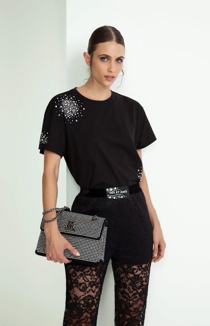 Woman wearing black crystal-studded t-shirt, lace pants, and holding a studded clutch bag