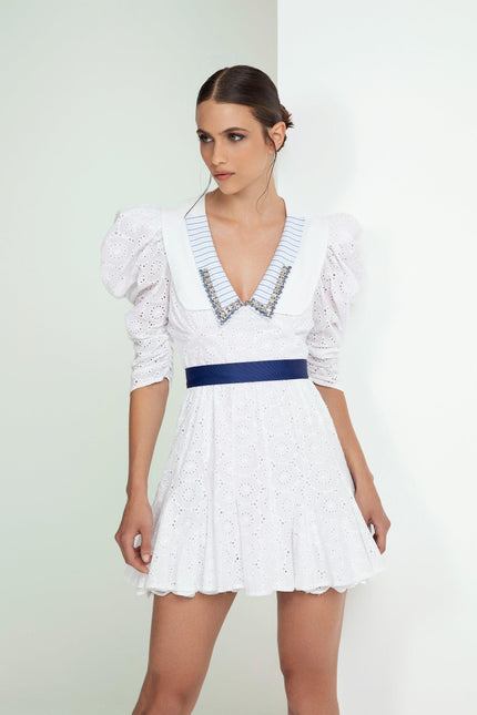 Woman wearing a white eyelet mini dress with puff sleeves, blue waistband, and striped collar