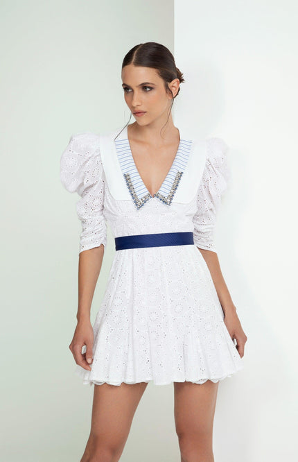 Woman wearing a white eyelet mini dress with puff sleeves, blue waistband, and striped collar