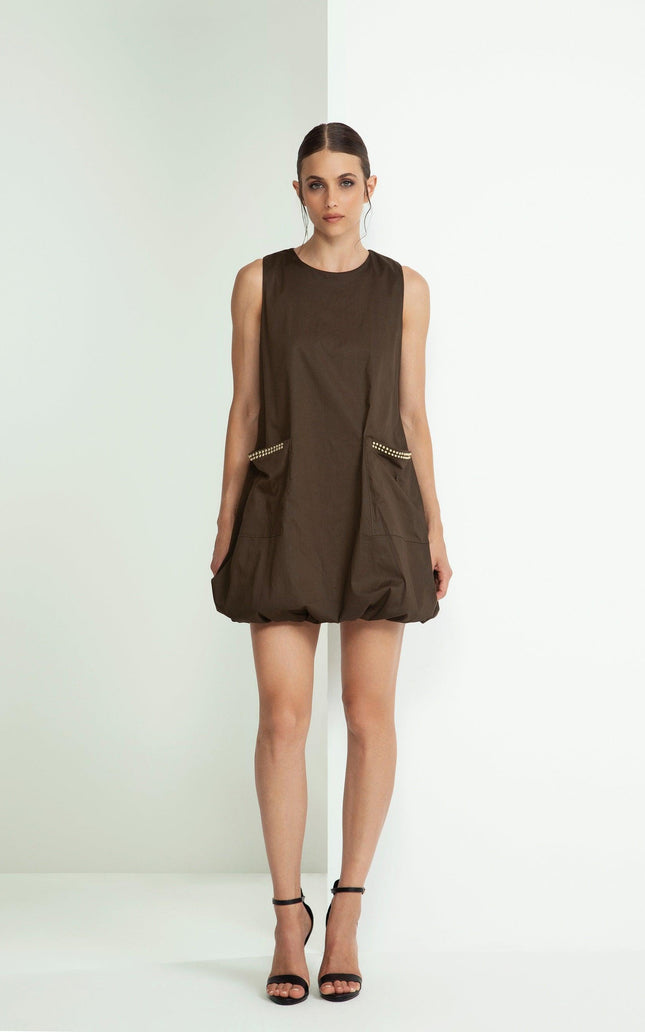 Woman in brown sleeveless mini dress with studded pockets, black heels, white background