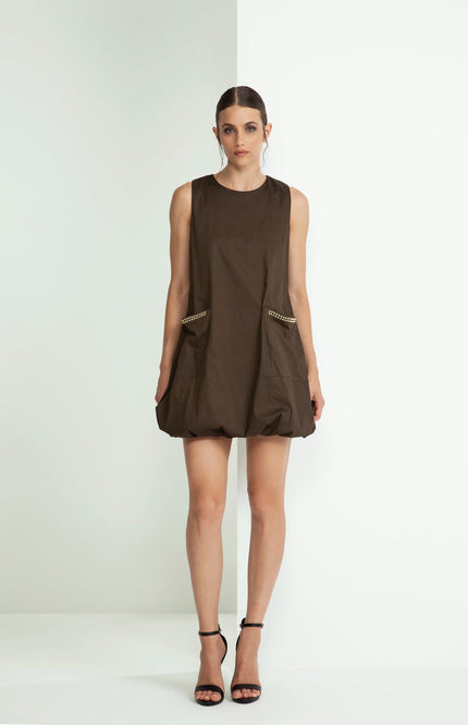 Woman in brown sleeveless mini dress with studded pockets, black heels, white background