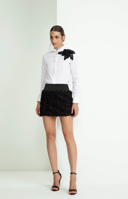 Woman in a white shirt with black floral embellishment and black textured mini skirt