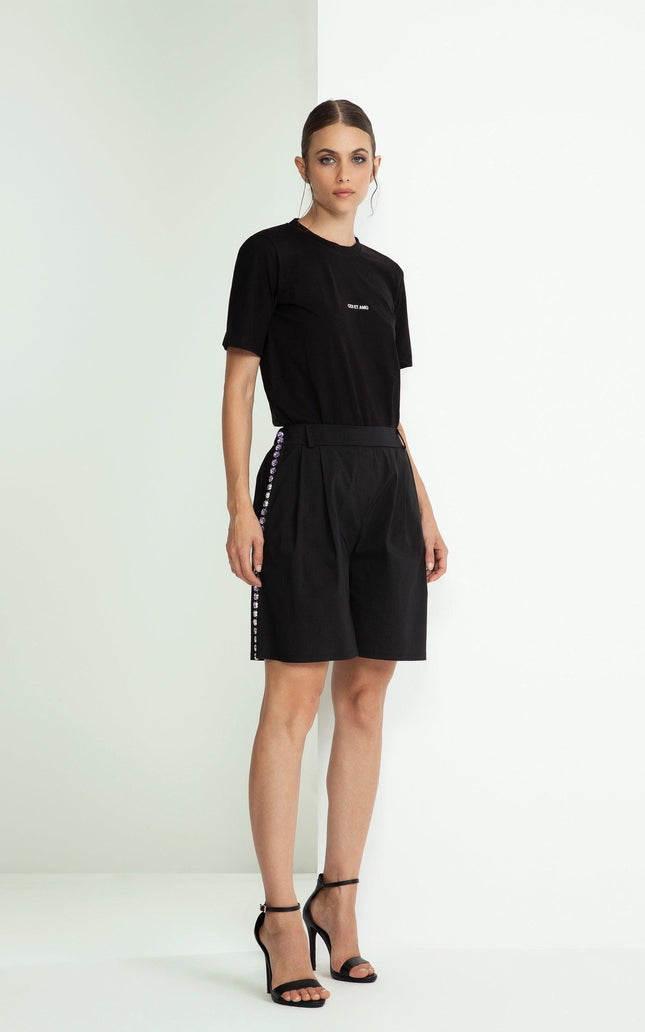 Woman in black t-shirt and high-waisted shorts with side button details, standing indoors