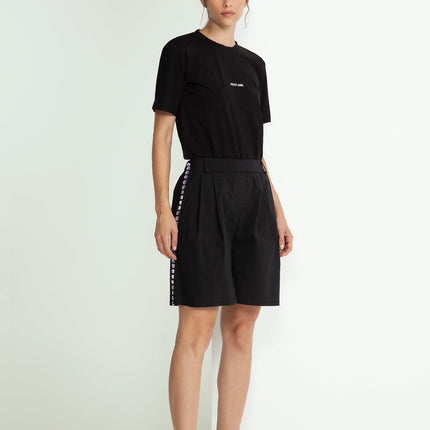 Woman in black t-shirt and high-waisted shorts with side button details, standing indoors