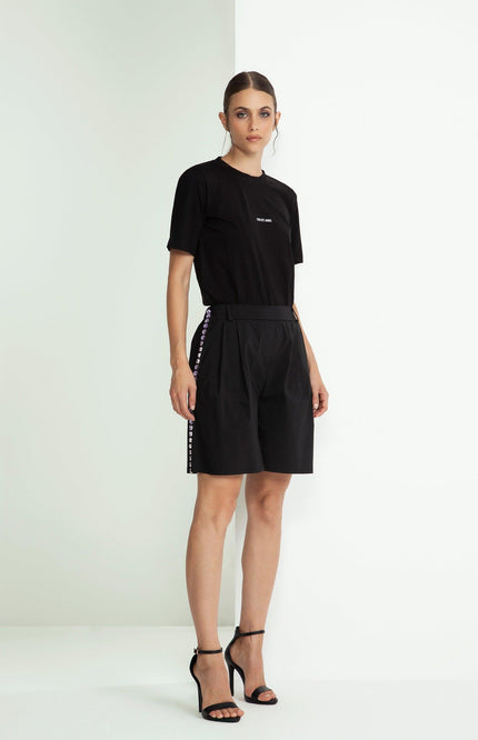 Woman in black t-shirt and high-waisted shorts with side button details, standing indoors