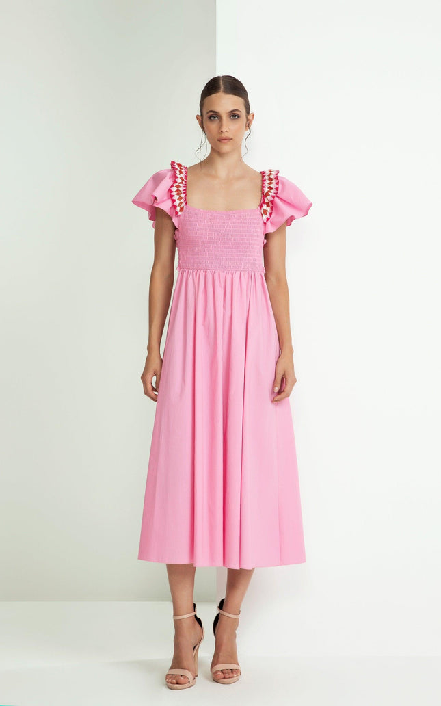 Woman in a pink midi dress with ruffled sleeves and ruched bodice, standing indoors