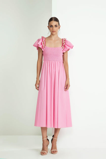 Woman in a pink midi dress with ruffled sleeves and ruched bodice, standing indoors