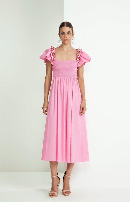 Woman in a pink midi dress with ruffled sleeves and ruched bodice, standing indoors