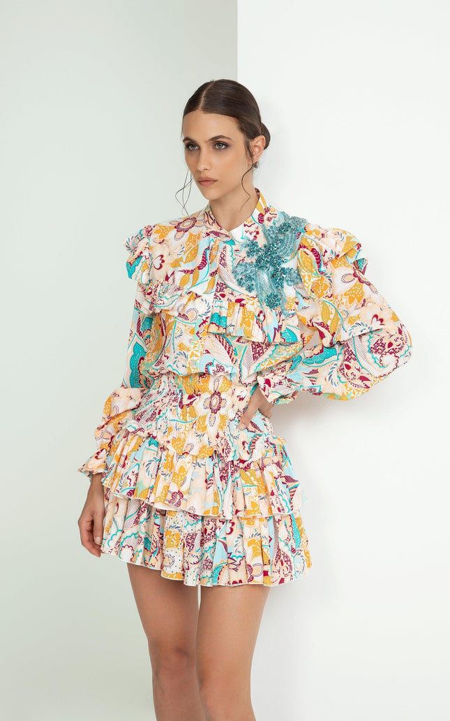 Woman wearing ruffled floral print mini dress with long sleeves and teal embellishment