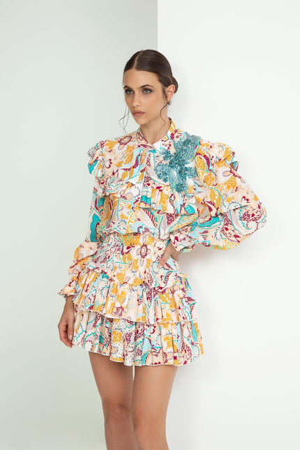 Woman wearing ruffled floral print mini dress with long sleeves and teal embellishment