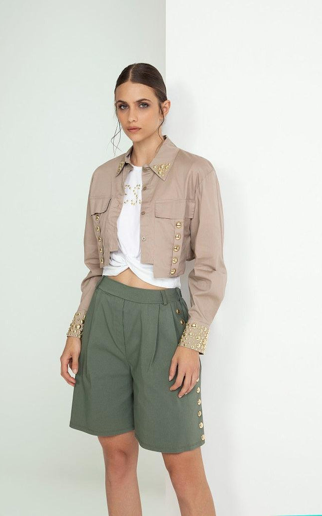 Woman wearing embellished cropped beige jacket, white knotted t-shirt, and green shorts