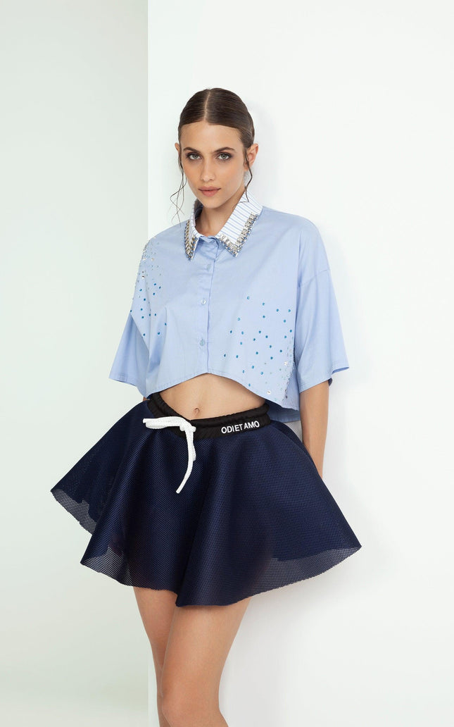Woman models blue embellished cropped shirt and flared navy mini skirt, modern fashion look